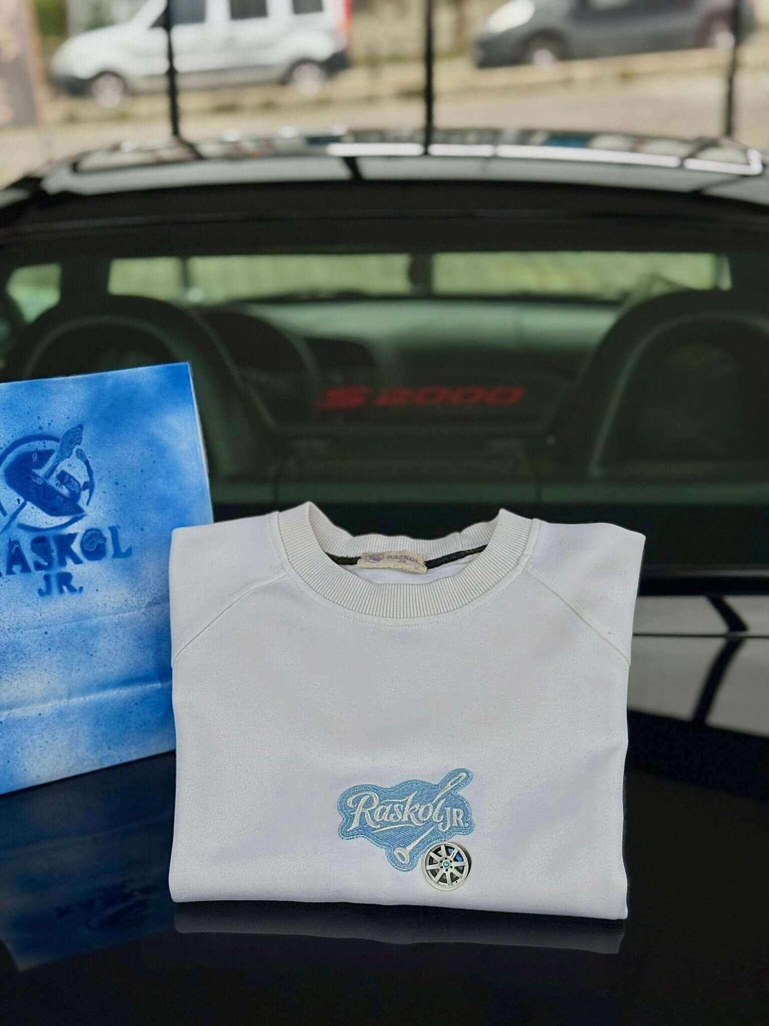 Raskol JR. Ekru Beyaz Mavi Denim&Jant Detaylı Sweatshirt folded on a car trunk with a blue shopping bag.