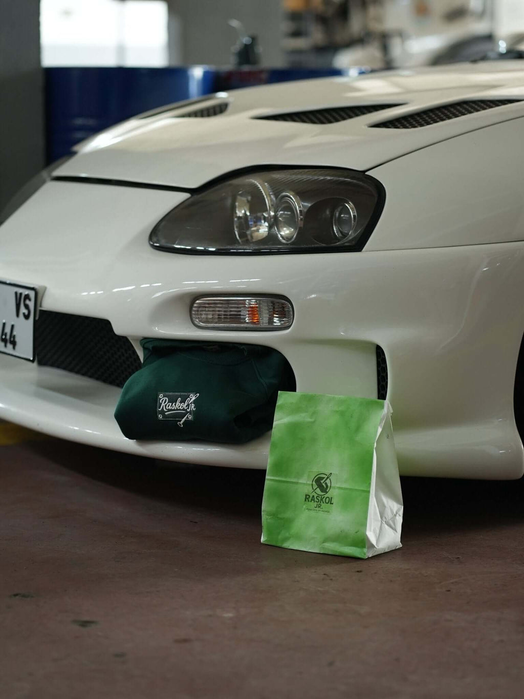 Raskol JR. Nefti Yeşil Sweatshirt displayed near a white sports car, showcasing its unique denim details.